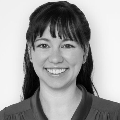 A person with long, dark hair styled elegantly, wearing a collared blouse, set against a plain white background.