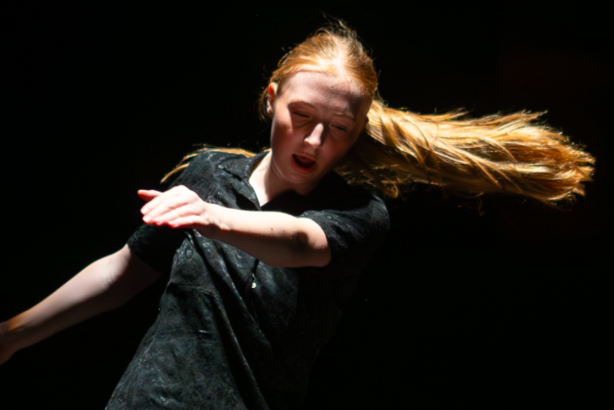 A dancer in a dark setting, captured mid-movement with flowing hair and an expressive pose, showcasing elegance and dynamism.